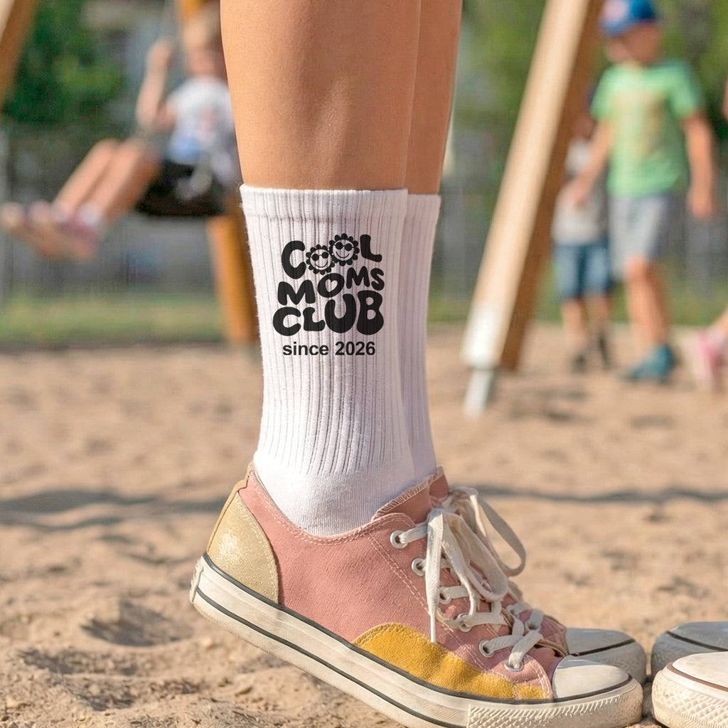 Weiße Tennissocken mit dem schwarzen Aufdruck Cool Moms Club und personalisierten Jahreszahlen am Knöchel, getragen in lässigen Sneakern.