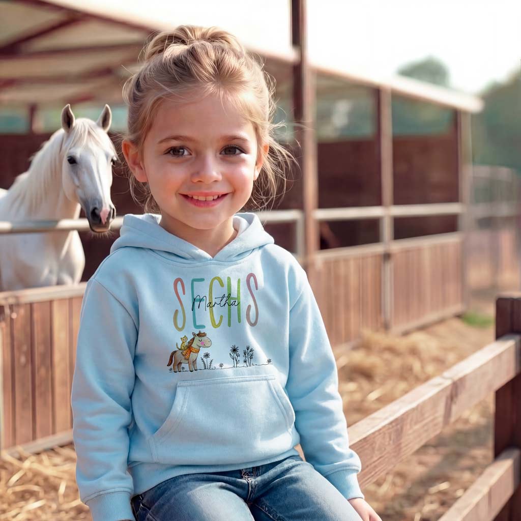 Hellblau-farbener Kinder-Kapuzenpullover mit Kängurutasche und hochwertigem Textildruck einer reitenden Katze auf einem Pony.