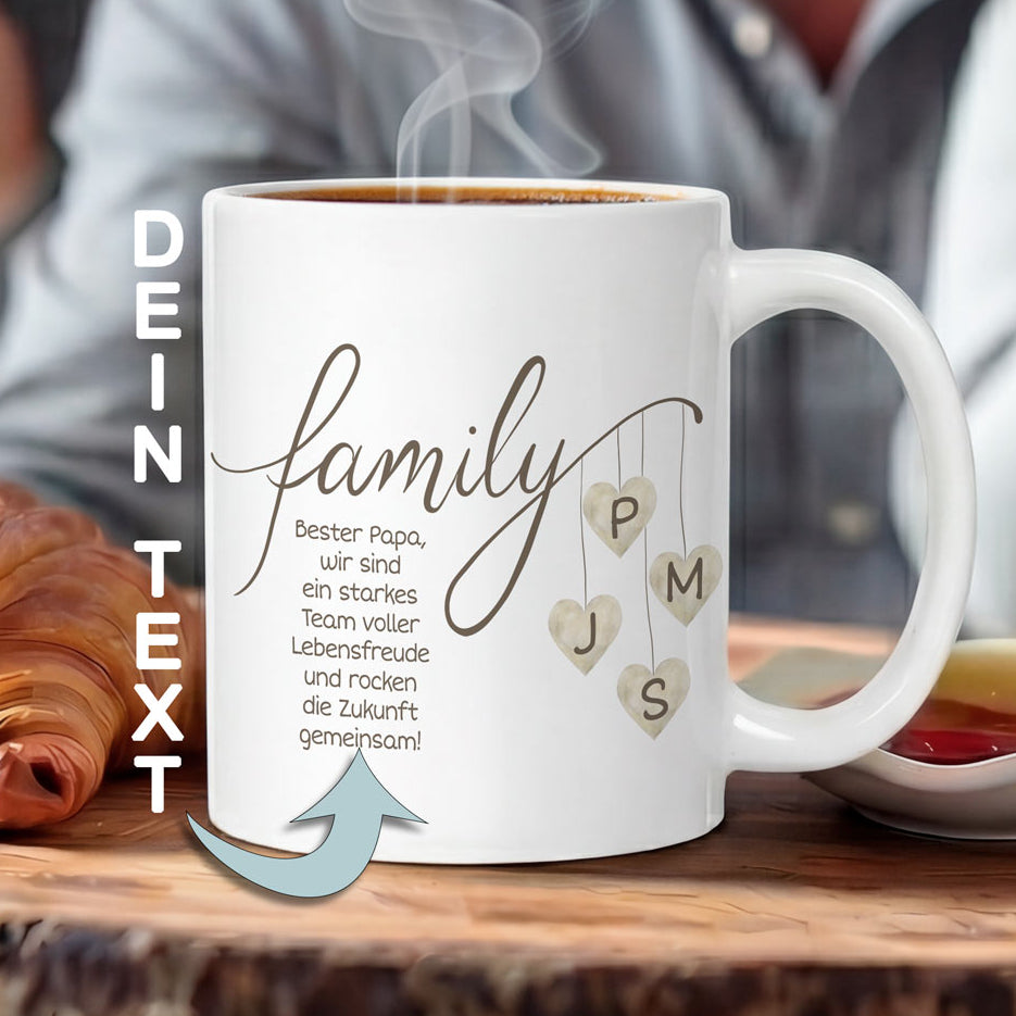 Eine minimalistische weiße Keramiktasse auf einem Holztisch, bedruckt mit dem Wort Family in dunkelbrauner Kalligrafie und beigen Aquarell-Herzen, die Initialen enthalten. Eine personalisierte Papa Tasse.