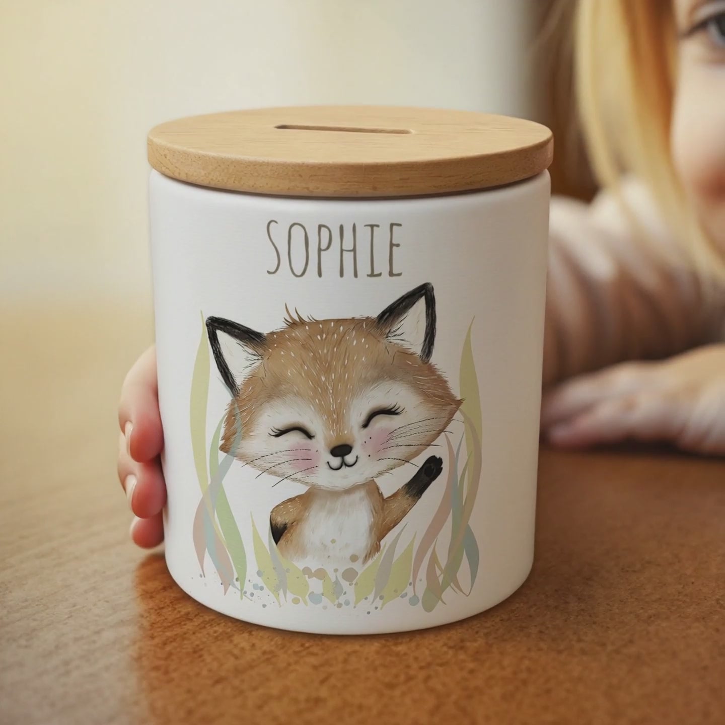 Ein kleines Mädchen winkt verträumt dem Fuchs-Motiv auf der Spardose zu